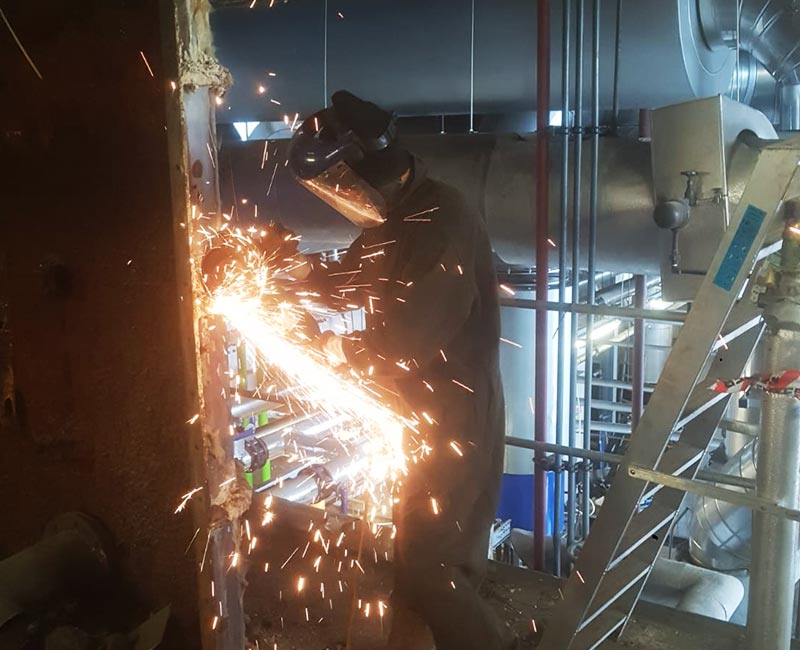 Man in safety equipment removing industrial boiler